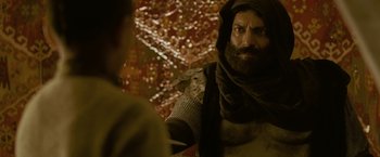 Movie still from “The Lovers” (2015), directed by Roland Joffé – A bearded man wearing a black scarf and a black robe; Close Up shot, Over the shoulder angle