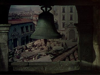 Movie still from “The Loves of Carmen” (1948), directed by Charles Vidor – A bell hanging in front of a painting of an old town; Wide shot, High angle