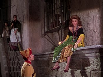 Movie still from “The Loves of Carmen” (1948), directed by Charles Vidor – A woman sitting on a stone ledge next to two men; Wide shot, High angle