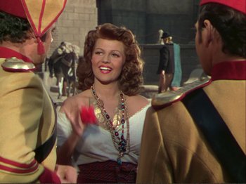 Movie still from “The Loves of Carmen” (1948), directed by Charles Vidor – A woman in a white top is talking to two men; Medium shot, Over the shoulder angle