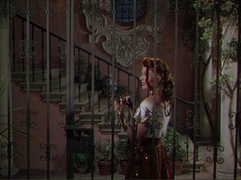 Movie still from “The Loves of Carmen” (1948), directed by Charles Vidor – A woman standing in front of a metal gate; Wide shot, Low angle