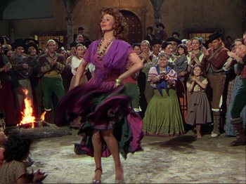 Movie still from “The Loves of Carmen” (1948), directed by Charles Vidor – A group of people watching a woman in a purple dress dance; Wide shot, Low angle