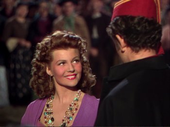 Movie still from “The Loves of Carmen” (1948), directed by Charles Vidor – A woman in a purple dress smiling at a man in a black suit; Medium shot, Over the shoulder angle