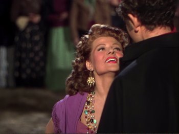 Movie still from “The Loves of Carmen” (1948), directed by Charles Vidor – A woman in a purple dress is standing next to a man in a black suit; Close Up shot, Over the shoulder angle