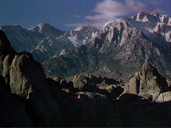 Movie still from “The Loves of Carmen” (1948), directed by Charles Vidor – A person standing on top of a rock in front of a mountain range; Extreme Wide shot, High angle