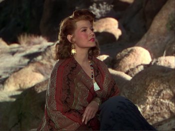Movie still from “The Loves of Carmen” (1948), directed by Charles Vidor – A woman sitting on top of a pile of rocks; Medium shot, Low angle