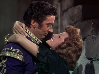 Movie still from “The Loves of Carmen” (1948), directed by Charles Vidor – A man and a woman embracing each other in front of a stone wall; Medium shot, Low angle