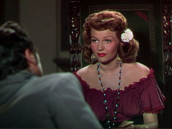 Movie still from “The Loves of Carmen” (1948), directed by Charles Vidor – A woman with a flower in her hair sitting in front of a man; Close Up shot, Over the shoulder angle