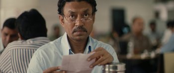Movie still from “The Lunchbox” (2013), directed by Ritesh Batra – A man with glasses holding a piece of paper in front of him; Close Up shot, Over the shoulder angle