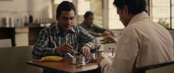 Movie still from “The Lunchbox” (2013), directed by Ritesh Batra – Two men are sitting at a table and one is putting something in a can; Medium shot, High angle