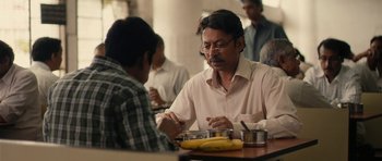 Movie still from “The Lunchbox” (2013), directed by Ritesh Batra – A man sitting at a table with a banana in front of him; Medium shot, Over the shoulder angle