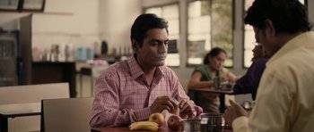 Movie still from “The Lunchbox” (2013), directed by Ritesh Batra – A man sitting at a table with a banana and apple; Medium shot, High angle