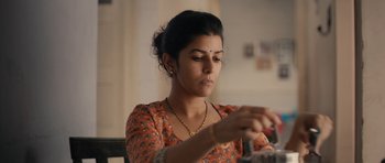 Movie still from “The Lunchbox” (2013), directed by Ritesh Batra – A woman in an orange shirt is looking down at her wrist; Close Up shot, Low angle