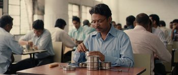 Movie still from “The Lunchbox” (2013), directed by Ritesh Batra – A man sitting at a wooden table with a lot of metal containers; Medium shot, Low angle