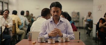 Movie still from “The Lunchbox” (2013), directed by Ritesh Batra – A man sitting at a table in front of a group of people; Medium shot, Low angle