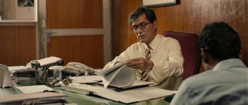 Movie still from “The Lunchbox” (2013), directed by Ritesh Batra – A man sitting at a desk looking at papers; Medium shot, High angle