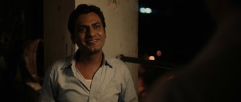Movie still from “The Lunchbox” (2013), directed by Ritesh Batra – A man smiling for the camera while standing next to a wall; Close Up shot, Over the shoulder angle