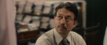 Movie still from “The Lunchbox” (2013), directed by Ritesh Batra – A man with glasses and a tie sitting in front of a stack of papers; Close Up shot, Over the shoulder angle