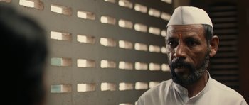 Movie still from “The Lunchbox” (2013), directed by Ritesh Batra – A man with a beard wearing a white hat; Close Up shot, Over the shoulder angle