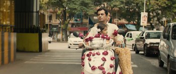 Movie still from “The Lunchbox” (2013), directed by Ritesh Batra – A man riding a scooter on the street with flowers on it; Wide shot, Over the shoulder angle
