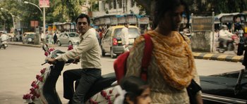 Movie still from “The Lunchbox” (2013), directed by Ritesh Batra – A man riding a motorcycle down a busy city street; Medium shot, Over the shoulder angle