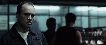 Movie still from “The Machinist” (2004), directed by Brad Anderson – A man in a uniform standing in front of a group of people; Close Up shot, Over the shoulder angle