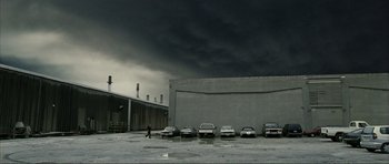 Movie still from “The Machinist” (2004), directed by Brad Anderson – A man walking in a parking lot next to a row of parked cars; Extreme Wide shot, Low angle