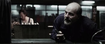 Movie still from “The Machinist” (2004), directed by Brad Anderson – A man with a beard and a mustache holding a pen; Medium shot, Low angle