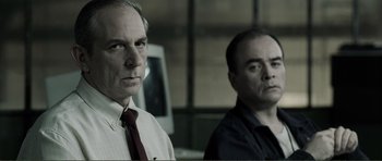 Movie still from “The Machinist” (2004), directed by Brad Anderson – Two men standing next to each other in front of a computer monitor; Close Up shot, Over the shoulder angle