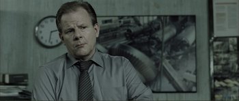 Movie still from “The Machinist” (2004), directed by Brad Anderson – A man wearing a gray shirt and a black tie in front of a picture; Close Up shot, Over the shoulder angle