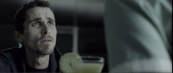 Movie still from “The Machinist” (2004), directed by Brad Anderson – A man sitting at a table with a drink in front of him; Close Up shot, Over the shoulder angle