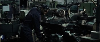 Movie still from “The Machinist” (2004), directed by Brad Anderson – A man working on a machine in an industrial setting; Medium shot, High angle