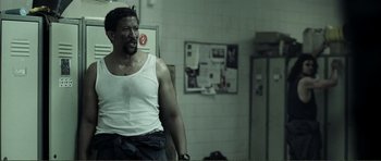 Movie still from “The Machinist” (2004), directed by Brad Anderson – A man in a white tank top is standing in a room; Medium shot, Over the shoulder angle