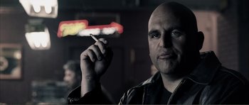 Movie still from “The Machinist” (2004), directed by Brad Anderson – A man with a shaved head is holding a cigarette; Close Up shot, Over the shoulder angle