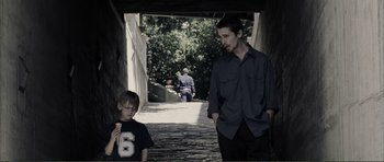 Movie still from “The Machinist” (2004), directed by Brad Anderson – A man and a boy are walking down a street; Medium shot, Over the shoulder angle