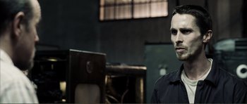Movie still from “The Machinist” (2004), directed by Brad Anderson – A man in a black shirt is standing in a room; Close Up shot, Over the shoulder angle