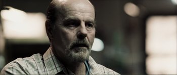 Movie still from “The Machinist” (2004), directed by Brad Anderson – An older man with a beard is looking into the distance; Close Up shot, Over the shoulder angle