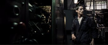 Movie still from “The Machinist” (2004), directed by Brad Anderson – A man standing next to a machine in a room; Medium shot, Low angle