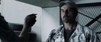 Movie still from “The Machinist” (2004), directed by Brad Anderson – A man with a baseball cap is looking into the camera; Close Up shot, Over the shoulder angle