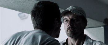 Movie still from “The Machinist” (2004), directed by Brad Anderson – A man with a beard and a hat is talking to another man; Close Up shot, Over the shoulder angle
