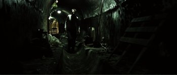 Movie still from “The Machinist” (2004), directed by Brad Anderson – A man standing inside of an underground cave; Wide shot, High angle