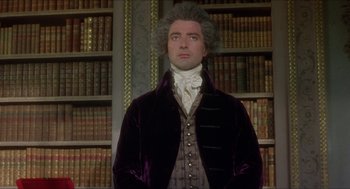 Movie still from “The Madness of King George” (1994), directed by Nicholas Hytner – A man in a purple jacket standing in front of a book shelf; Medium shot, Low angle