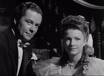 Movie still from “The Magnificent Ambersons” (1942), directed by Robert Wise – A man and a woman pose for a picture in formal wear; Close Up shot, Low angle