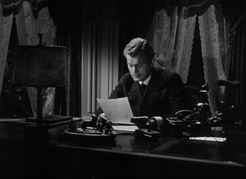 Movie still from “The Magnificent Ambersons” (1942), directed by Robert Wise – A man sitting at a desk looking at papers; Medium shot, Low angle