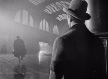 Movie still from “The Magnificent Ambersons” (1942), directed by Robert Wise – A man in a hat is walking through a train station; Wide shot, Low angle