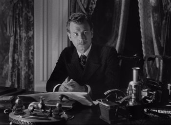 Movie still from “The Magnificent Ambersons” (1942), directed by Robert Wise – A man sitting at a desk in front of papers; Medium shot, Low angle