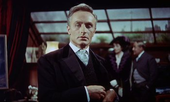 Movie still from “The Man Who Could Cheat Death” (1959), directed by Terence Fisher – A man in a suit and tie standing in front of a building; Medium shot, Low angle