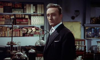 Movie still from “The Man Who Could Cheat Death” (1959), directed by Terence Fisher – A man wearing a suit and tie standing in front of a bookshelf; Medium shot, Low angle