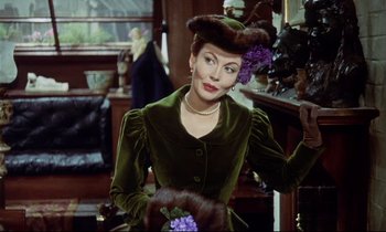 Movie still from “The Man Who Could Cheat Death” (1959), directed by Terence Fisher – A woman in a green dress holding a bouquet of flowers; Medium shot, Over the shoulder angle