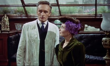 Movie still from “The Man Who Could Cheat Death” (1959), directed by Terence Fisher – An older man standing next to an older woman in front of a window; Medium shot, Low angle
